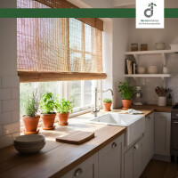Helle Landhausküche mit weißer Spüle, Holzarbeitsplatte und Kräutertöpfen auf der Fensterbank. Vor dem großen Fenster filtert eine Schilfjalousie das warme Sonnenlicht, während offene Regale mit Geschirr den Raum ergänzen. Oben rechts ist das Logo DE-COmmerce zu sehen.