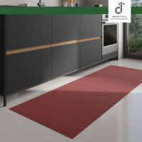 Moderner Küchenbereich mit dunklen Unterschränken und integriertem Backofen; auf dem hellen Boden liegt ein langer, rechteckiger Läufer aus Bambus in einem warmen rot. Rechts fällt Tageslicht durch ein großes Fenster ein. Oben rechts ist das DE-COmmerce Logo.