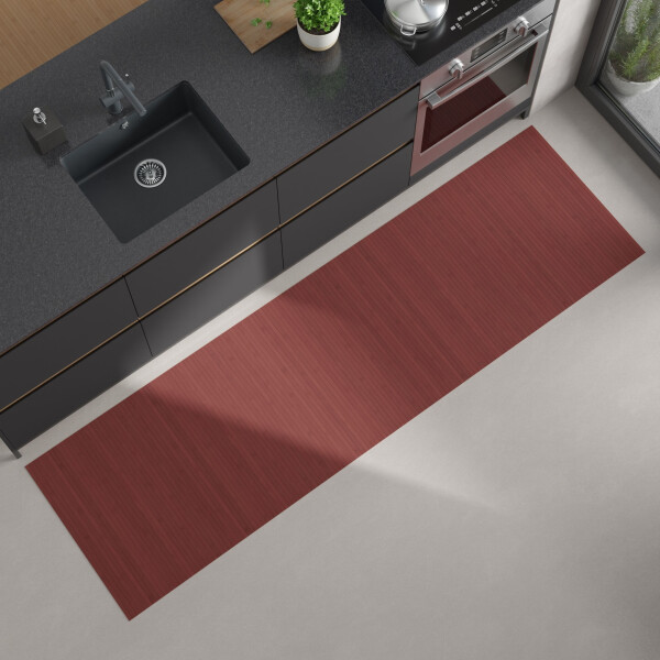 Moderne Küchenansicht von oben mit dunkler Arbeitsplatte, eingebautem schwarzen Spülbecken und Herd; auf dem hellen Boden liegt ein langer, rechteckiger Bambus-Küchenläufer in einem warmen Rotton.