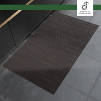 Rechteckiger, schwarzbrauner Bambusläufer mit feinen Längsstreifen liegt auf einem grauen Steinboden vor modernen, dunklen Küchenunterschränken. Oben rechts befindet sich das DE-COmmerce Logo.