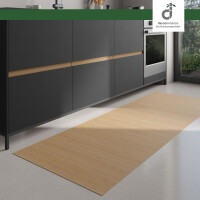 Moderner Küchenbereich mit dunklen Unterschränken und integriertem Backofen; auf dem hellen Boden liegt ein langer, rechteckiger Läufer aus hellem Bambus. Rechts fällt Tageslicht durch ein großes Fenster ein. Oben rechts ist das DE-COmmerce Logo.