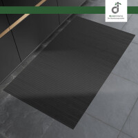 Rechteckiger, bläulich grauer Bambusläufer mit feinen Längsstreifen liegt auf einem grauen Steinboden vor modernen, dunklen Küchenunterschränken. Oben rechts befindet sich das DE-COmmerce Logo.