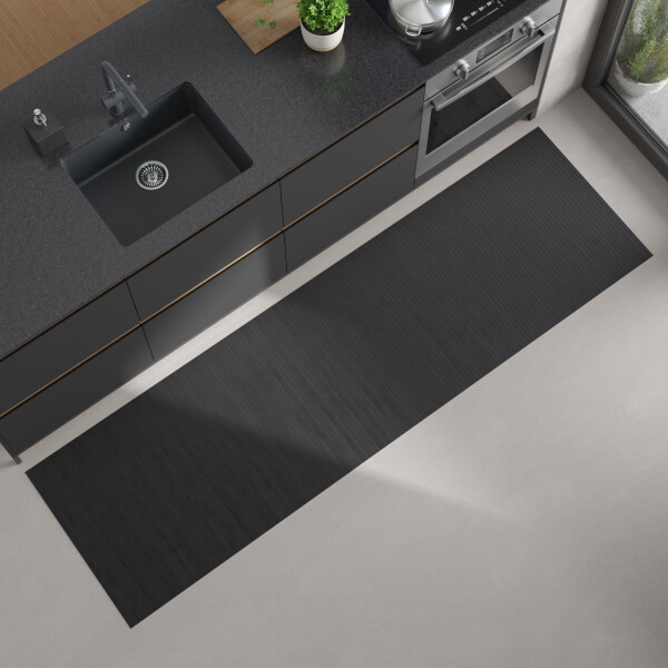Moderne Küchenansicht von oben mit dunkler Arbeitsplatte, eingebautem schwarzen Spülbecken und Herd; auf dem hellen Boden liegt ein langer, rechteckiger, bläulich grauer Bambus-Küchenläufer.