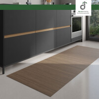 Moderner Küchenbereich mit dunklen Unterschränken und integriertem Backofen; auf dem hellen Boden liegt ein langer, rechteckiger Läufer aus hellgrau-braunen Bambus. Rechts fällt Tageslicht durch ein großes Fenster ein. Oben rechts ist das DE-COmmerce Logo.