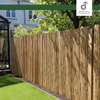 Natürlicher Bambus-Windschutzzaun in Rindenmulch entlang eines Gartens mit grünem Rasen, daneben ein modernes Glashaus und schattenspendende Bäume; oben rechts das DE-COmmerce Logo.