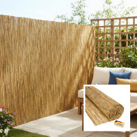 Helle Terrasse mit Schilf-Sichtschutzmatte entlang der rechten Seite; Holzsofa mit weißen Polstern und blau-gelben Kissen, Holztisch mit Tasse, Buch und Sukkulenten, im Hintergrund Rankgitter und blühende Pflanzen.