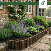 Gartenbeet entlang einer Backsteinwand mit Spalier und blühenden Kletterrosen, bepflanzt mit Lavendel, Stauden und Hostas, eingefasst von einer niedrigen Bambus-Beeteinfassung neben einem geschwungenen Natursteinweg mit Kies; oben rechts DE-COmmerce Logo.