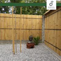 Kleiner Zen-Garten mit weißem Kiesboden, umgeben von Bambus-Sichtschutzwänden; in der Mitte eine Buddha-Statue auf einem Sockel, daneben eine kleine Palme und mehrere aufrechtstehende Bambusstangen, im Hintergrund grüne Bäume; oben rechts das DE-COmmerce Logo.