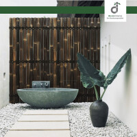 Moderner Außenbereich mit einem runden, grauen Steinwaschbecken vor einer vertikalen Bambuswand. Der Boden ist mit weißen Kieselsteinen bedeckt, ein schlichter Steinweg führt zum Becken. Rechts steht eine dunkle Vase mit großen, grünen Blättern vor einer weißen Wand; oben rechts das DE-COmmerce Logo.