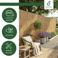 Natürliche Schilfmatte als Sichtschutz auf einer Terrasse mit kleiner Sitzgruppe, dekorativer Lichterkette, Rankpflanzen und bepflanzten Blumentöpfen. Oben rechts befindet sich das DE-COmmerce Logo.