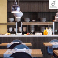 Modern eingerichteter Restaurant-/ Bistrobereich mit schwarzbraunem Bambus-Wandbelag, offenen Regalen mit Geschirr, Buffettheke mit Getränken und Speisen sowie gedeckten Holztischen und dunkelblauen Stühlen, oben rechts ist das DE-COmmerce Logo.