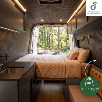 Gemütlicher Campervan mit schwarzbraunem Bambus-Wand- und Deckenbelag, Doppelbett und kompakter Küche; durch die geöffneten Hecktüren fällt der Blick in einen grünen Wald. Eine Grafik weist auf das geringe Gewicht des Wandbelags von ca. 1,70 kg/m² hin, oben rechts das DE-COmmerce Logo.