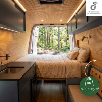 Gemütlicher Campervan mit warmem Bambus-Wand- und Deckenbelag, Doppelbett und kompakter Küche; durch die geöffneten Hecktüren fällt der Blick in einen grünen Wald. Eine Grafik weist auf das geringe Gewicht des Wandbelags von ca. 1,70 kg/m² hin, oben rechts das DE-COmmerce Logo.